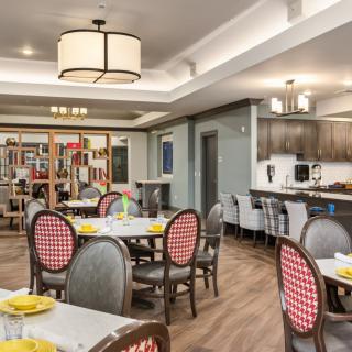 A well-furnished dining room with tables set for a meal and a kitchen area in the background.