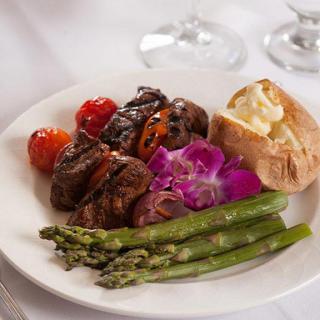 A gourmet meal featuring steak, asparagus, cherry tomatoes, and a baked potato served on a fine dining plate.