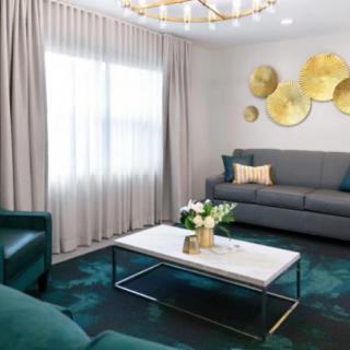A stylish modern living room featuring a gray sofa, marble coffee table, elegant curtains, and decorative wall art with gold accents.