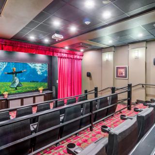 A cozy home theater setup with tiered seating, a projector screen displaying a movie scene, and ambient lighting.