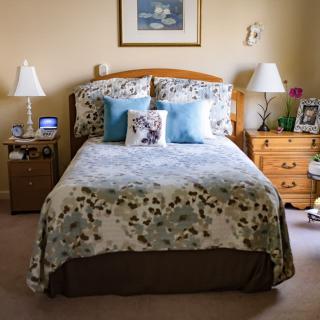 A cozy bedroom with a neatly made bed, flanked by nightstands and lamps, decorated with pillows and artwork.