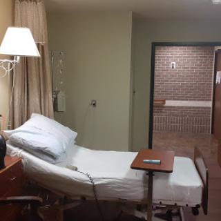 A view of a hospital patient room featuring an adjustable bed and nearby amenities.