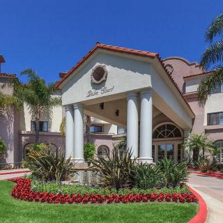 A picturesque entrance of a building featuring columns, surrounded by lush landscaping and palm trees.