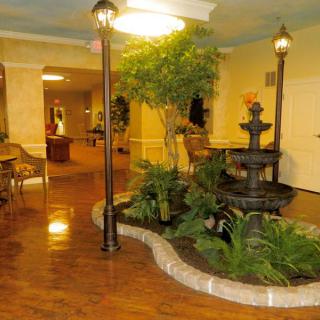 A hotel lobby featuring a central fountain surrounded by plants and seating areas, illuminated by lamppost-style lighting.