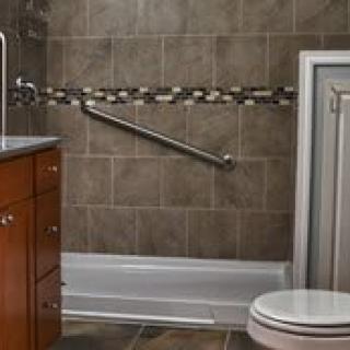 A modern bathroom featuring a toilet, sink, tiled walls, and a shower with a grab bar.