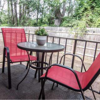 A cozy patio with red chairs and a small round table, set against a wooden fence surrounded by trees.