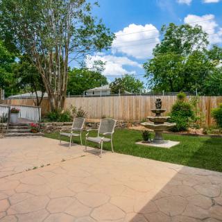 A serene backyard featuring a patio with chairs, a beautiful fountain, and lush greenery.