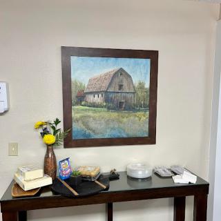 A cozy interior space featuring a landscape painting of a barn, accompanied by a decorative vase with flowers.