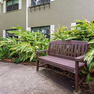 A wooden bench placed alongside a garden path with lush greenery in front of a building.