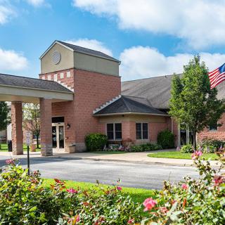 A healthcare clinic with a brick exterior and surrounding landscaping, featuring an American flag in the foreground.