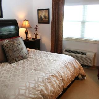 A cozy bedroom featuring a neatly made bed with decorative pillows, a bedside lamp, and framed artwork on the wall.
