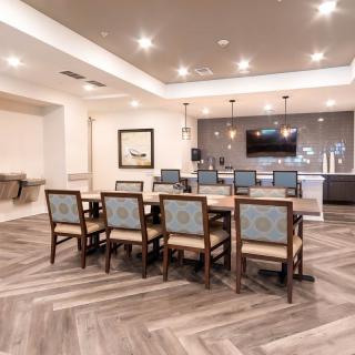 A modern dining room featuring a large table, stylish chairs, and herringbone flooring, complete with a bar area and television.