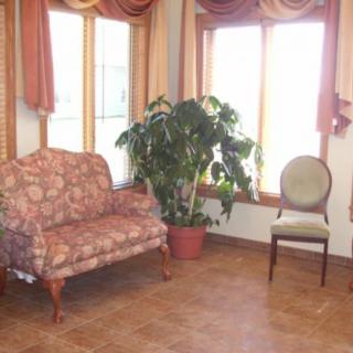 A cozy living room with a floral sofa, a single chair, and a potted plant near large windows with curtains.