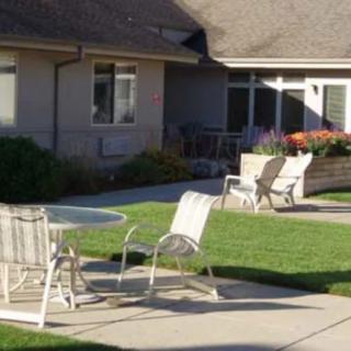 A serene outdoor patio area with chairs and a table, surrounded by a well-maintained lawn and garden.