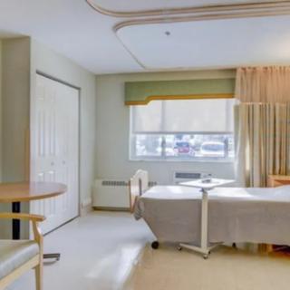 A clean and well-lit hospital room featuring a bed, side table, and large window with curtains.