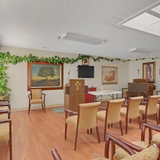 A small chapel interior with rows of chairs, a podium, and artwork on the walls.