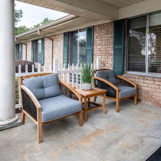 A cozy patio setup with two cushioned chairs and a small table with a plant, set against a brick wall with windows.