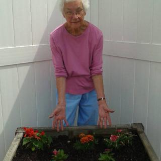 An elderly person showing their flower garden with a smile.