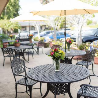 A peaceful outdoor patio area with tables, chairs, and floral arrangements under large umbrellas.