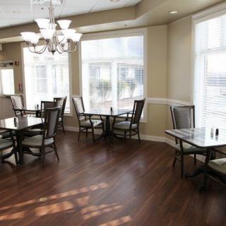 A sunlit dining area featuring elegant tables and chairs, wooden flooring, and a decorative chandelier.