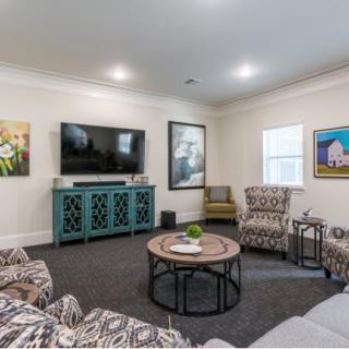 A cozy living room featuring a television, patterned chairs, and vibrant artwork on the walls.
