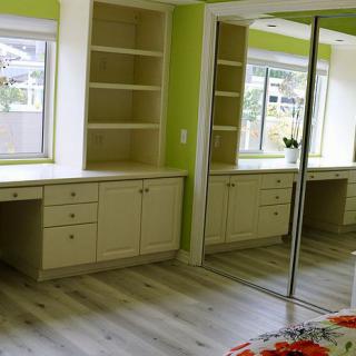 A bright room with built-in desks and shelves, large mirrored closet doors, and green walls.
