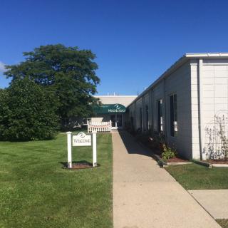 A pathway leading to a building with a green awning, surrounded by grass and trees under a clear blue sky.