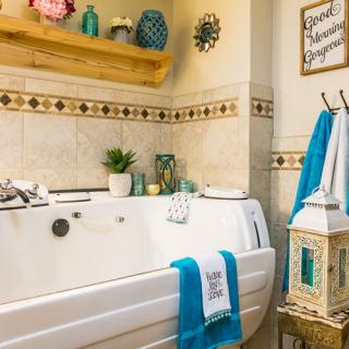 A cozy bathroom featuring a white bathtub adorned with turquoise towels, decorative plants, and wall accents.