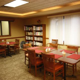 A cozy dining area with tables, chairs, and a bookshelf filled with books.
