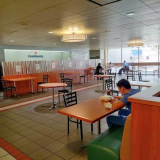 A spacious cafeteria with tables and chairs, featuring a few individuals dining.