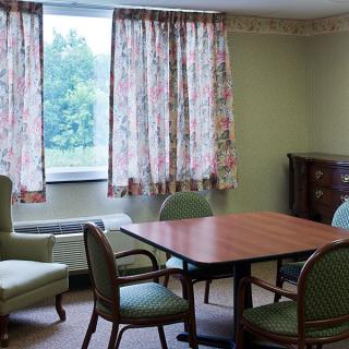 A cozy room with a wooden table surrounded by chairs and floral curtains on the windows.