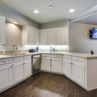A modern kitchen with white cabinets, hardwood flooring, and stainless steel appliances.