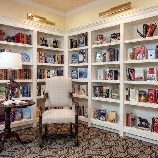 A cozy corner in a library with bookshelves filled with various books, an inviting reading chair, and a lamp providing warm light.