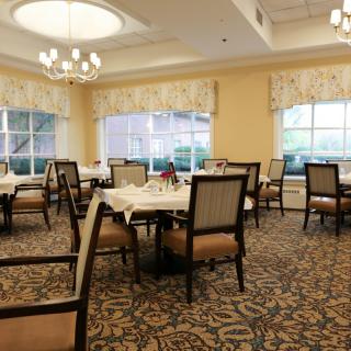 An elegant dining room with neatly arranged tables and chairs, large windows, and a chandelier.