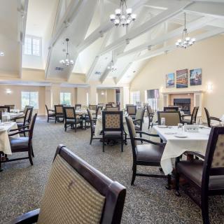 A spacious and elegantly decorated dining room with neatly arranged tables and chairs under a bright ceiling with chandeliers.