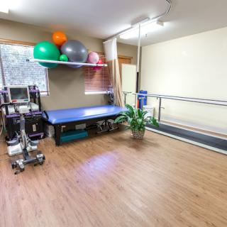 A well-equipped physical therapy room with parallel bars, exercise balls, and a treatment table.