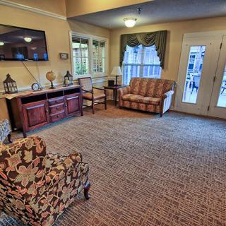 A cozy living room featuring patterned chairs, a sofa, and large windows with decorative curtains.