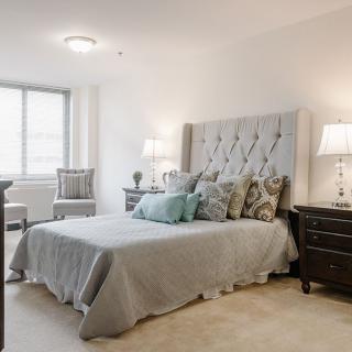 A modern bedroom featuring a plush bed with decorative pillows, two nightstands with lamps, and a large window allowing natural light.