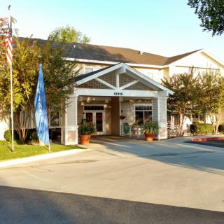 The entrance of a building with flags, surrounded by trees and a driveway.