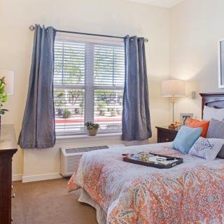 A cozy bedroom with a neatly made bed, soft lighting, and a large window with blue curtains.