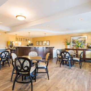 A cozy cafe with wooden flooring, featuring a bistro-style seating area with tables and chairs.