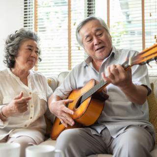 An elderly couple enjoying a musical moment together as the man plays the guitar in their cozy living room.