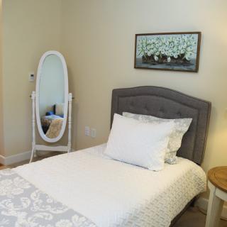 A cozy bedroom with a single bed, decorative pillow, and a standing mirror, plemented by framed artwork and a side table.