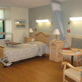A well-lit hospital room with a single bed and comfortable seating.