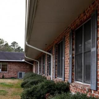 A brick residential house with blue shutters, gutters, and bushes lining the exterior.