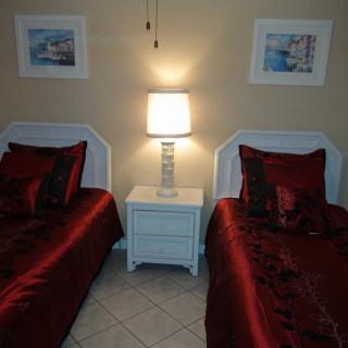 A cozy bedroom with twin beds adorned in red bedding, a shared white nightstand, and soft lighting from a table lamp.