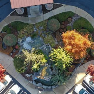 Aerial view of a beautifully landscaped garden with vibrant autumn foliage, bordered by a parking area.