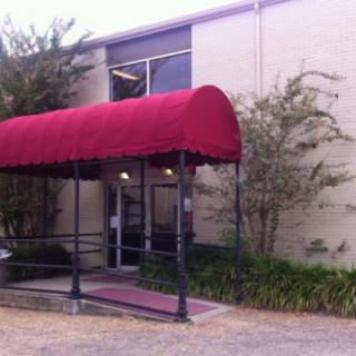 A building entrance with a red awning and surrounding greenery.
