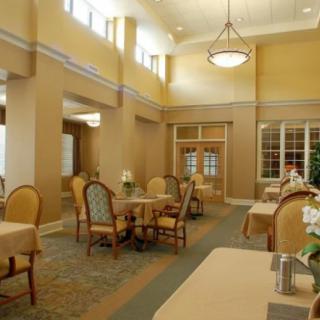 A well-lit dining area with multiple tables and chairs, featuring large windows and warm lighting.