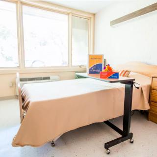 A clean and organized hospital room with a bed, adjustable table, and medical supplies near a window.